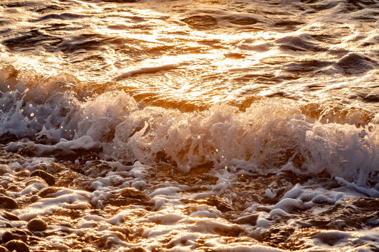 dettaglio di un onda che si infrange nella battigia di una spiaggia al tramonto 