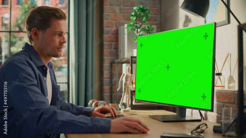 Poster Young Handsome Man Working from Home on Desktop Computer with Green Screen Mock Up Display. Creative Male Checking Social Media, Browsing Internet. Living Room in Bright Loft Apartment. Static Shot.