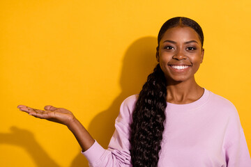 Portrait of charming positive girl arm palm hold demonstrate empty space isolated on yellow color...