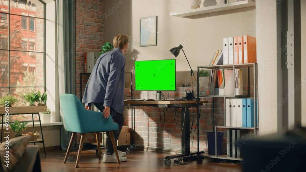 Poster young handsome man sitting down to work from home on desktop computer with green screen mock up disp