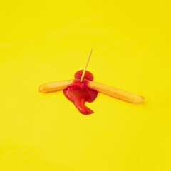 creative minimal composition of killed french fries with wooden toothpick from which it leaks ketchup on yellow background.