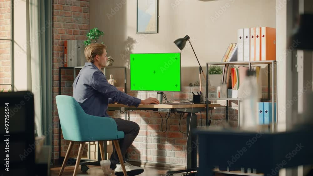 Poster young handsome man working from home on desktop computer with green screen mock up display. male che