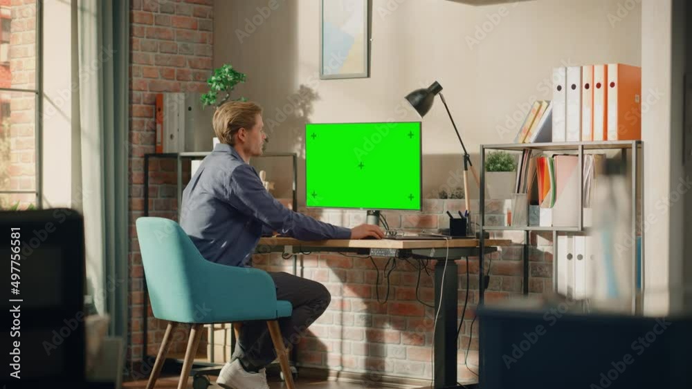 Poster young handsome man working from home on desktop computer with green screen mock up display. male che