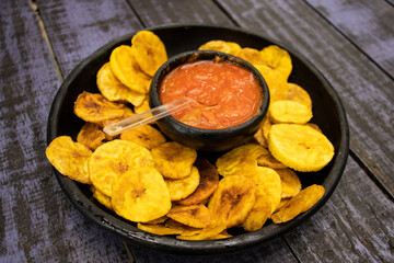 Plantain chips served with Colombian traditional hogao on top of a wooden table