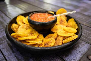 Plantain chips served with Colombian traditional hogao on top of a wooden table
