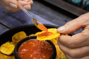 Closeup of woman's hands while eating plantain chips served with Colombian traditional hogao © anamejia18