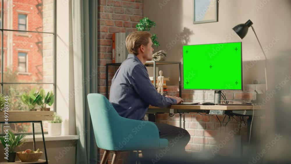 Poster Young Handsome Man Working from Home on Desktop Computer with Green Screen Mock Up Display. Creative Male Checking Social Media, Browsing Internet. Living Room in Bright Loft Apartment. Static Shot.