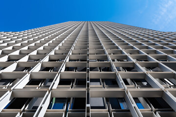 Facade of a modern office tower with vanishing point from frog perspective with bright sunlight on a blue sky day. Lines and structures in perfect symmetry. - obrazy, fototapety, plakaty