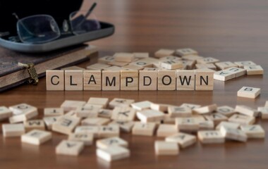 clampdown word or concept represented by wooden letter tiles on a wooden table with glasses and a book