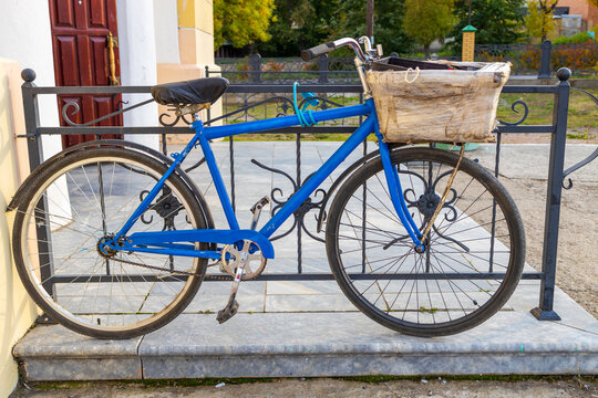 an old blue bicycle with a basket in front stands and a fence in front of the store