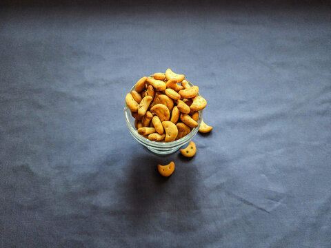 Stock photo of testy crunchy salted masala cashew shape biscuit kept in transparent glass bowl on dolphin gray color background. Picture captured under bright light at Bangalore, Karnataka, India.