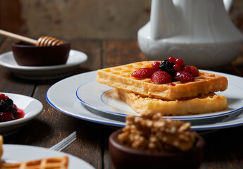 Breakfast waffles served with strawberries, blueberries, raspberries, honey, nuts and a teapot