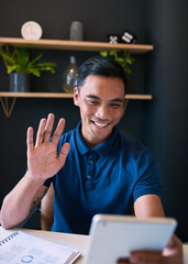A young Asian man waves to a colleague on a digital tablet in the office