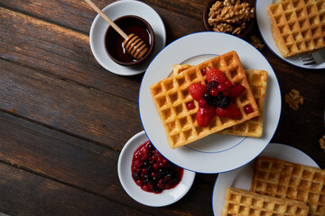 Breakfast waffles served with strawberries, blueberries, raspberries, honey, nuts on a wooden table. Top view