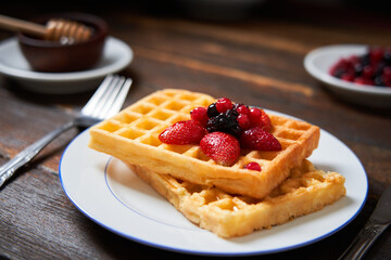 Fresh waffles on a plate with berries and honey on a wooden table. Copy space