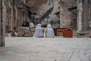Two religious Ethiopian women in white headscarves sit on a stone step in the old city of...