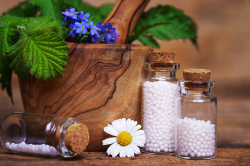 Bottles of globuli. Homeopathic remedies. Flowers and leaves in the mortar and on table. Homeopathy...