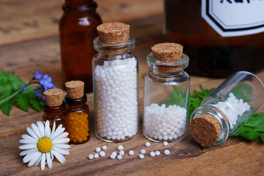Medical glas vials on wooden table, filled with globulis. Decoratet with leaves and flowers.