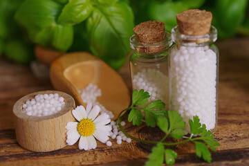 Medical glas vials on wooden table, filled with globulis. Decoratet with leaves and flowers. Homeopathy conzept.