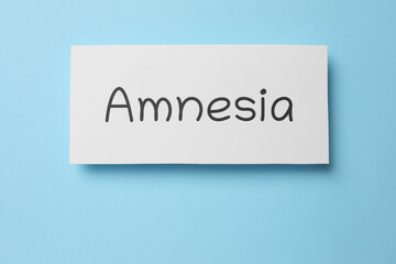 Fototapeta premium Card with word Amnesia on light blue background, top view