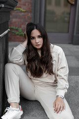 A girl in a white tracksuit on a city street on a sunny clear day walks posing for the camera sits on the steps of the hotel building near the column