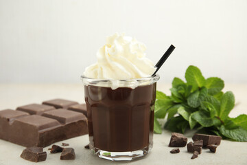 Glass of delicious hot chocolate with whipped cream, chunks and fresh mint on light table