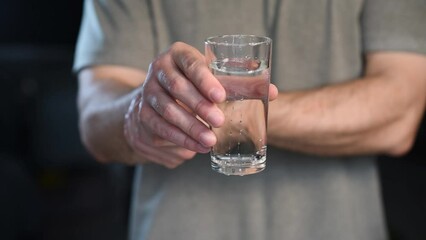 Tremor of the hands when trying to drink. Water splashes from a glass in the hand of a man with tremors, Parkinson's disease.