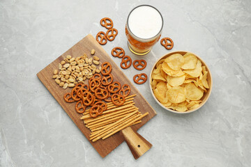 Glass of beer served with delicious pretzel crackers and other snacks on light grey table, flat lay