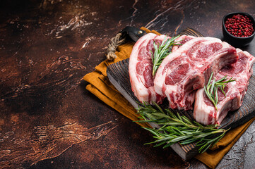 Raw fresh saddle of lamb mutton with herbs and spices on butcher board. Dark background. Top view....