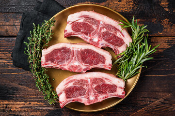Uncooked Raw lamb loin chops steaks, saddle in plate with rosemary and thyme. Wooden background. Top view