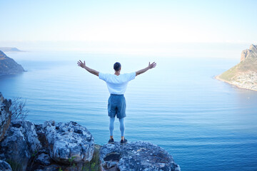 This is freedom. Rearview shot of an unrecognizable young man standing with his arms outstretched while looking at the ocean view from the mountain.