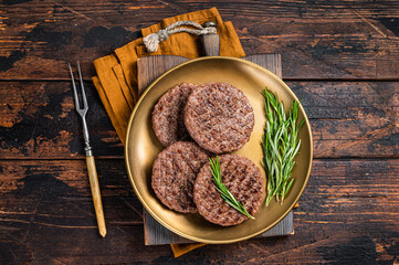 Grilled burger beef meat patty with herbs and spices on steel plate. Wooden background. Top view