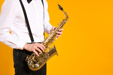 Obraz premium Man in elegant outfit with saxophone on yellow background, closeup. Space for text