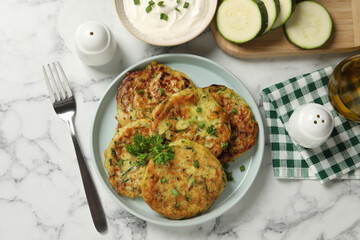 Delicious zucchini fritters served on white marble table, flat lay