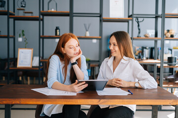 Front view of two relaxed young business women working using digital tablet at meeting desk with...