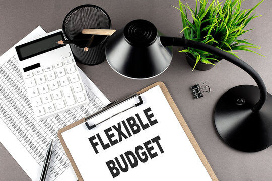 Clipboard ,chart and calculator, lamp and workspace accessories on a grey table. Top view , text FLEXIBLE BUDGET