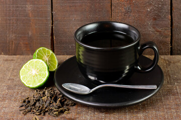 Bergamot tea or Earl Grey tea in black cup and fresh bergamot fruit with sliced on black wooden table.