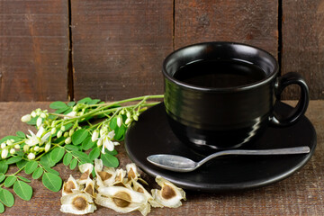 Moringa Tea in black cup with fresh green leaf and seed on rustic wooden background. Moringa oleifera tropical herb healthy lifestyle concept.