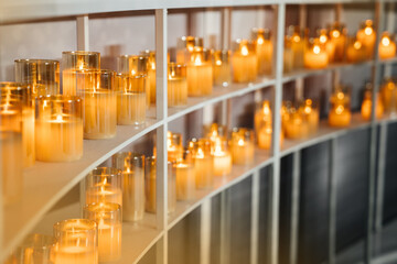 A lot of electric candles in glass cups stand on the shelves and decorate the wedding ceremony. Soft blur and focus. Warm calm design.