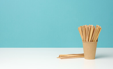 disposable paper cups and wooden sticks on white table, blue background