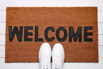 New clean mat with word WELCOME and shoes on floor, top view