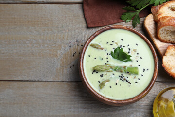 Bowl of delicious asparagus soup served on wooden table, flat lay. Space for text