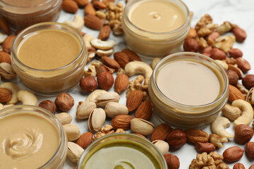 Jars with butters made of different nuts and ingredients on white marble table, closeup