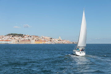 White Yacht sailing in Tagus river with Lisbon cityscape on the background, Portugal