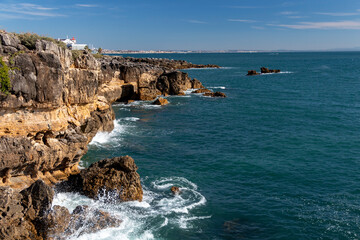 View of the Atlantic Ocean coastline and Pedra da Nau rock, rocky coastal area in Cascais on a sunny day, Portugal