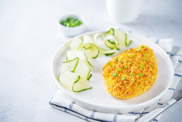 Bread crumbs cheesy chicken breast with cucumbers in a plate