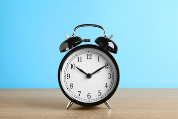 Black alarm clock on wooden table against light blue background