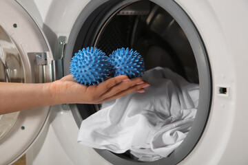 Woman putting blue dryer balls into washing machine, closeup