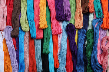 Different colorful embroidery threads as background, top view