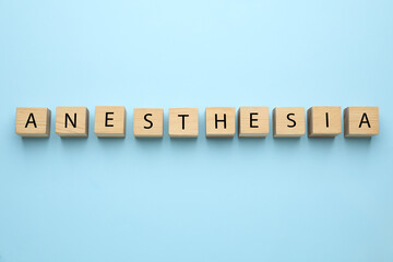 Wooden cubes with word Anesthesia on light blue background, top view